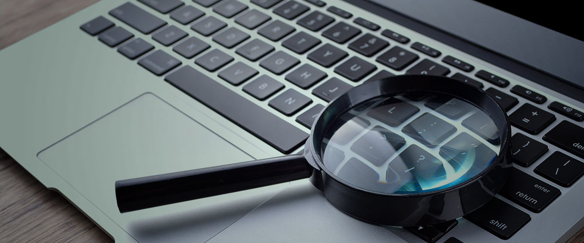 Lupa sobre teclado representa a pesquisa de informações para localizar uma pessoa